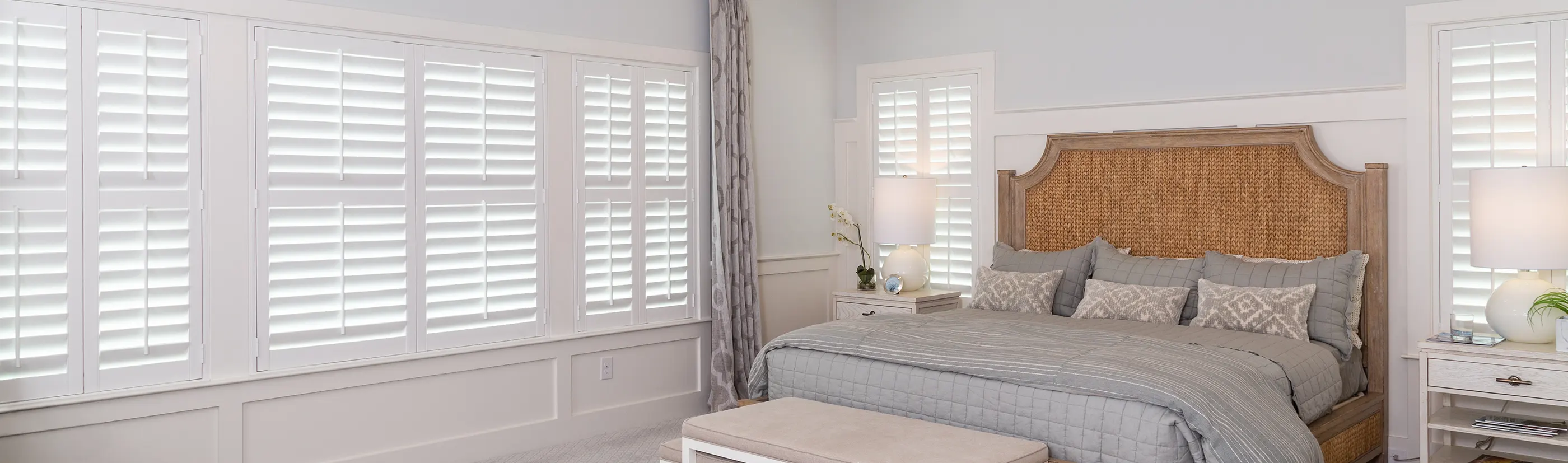 Closed Polywood shutters on several bedroom windows in a modern gray bedroom